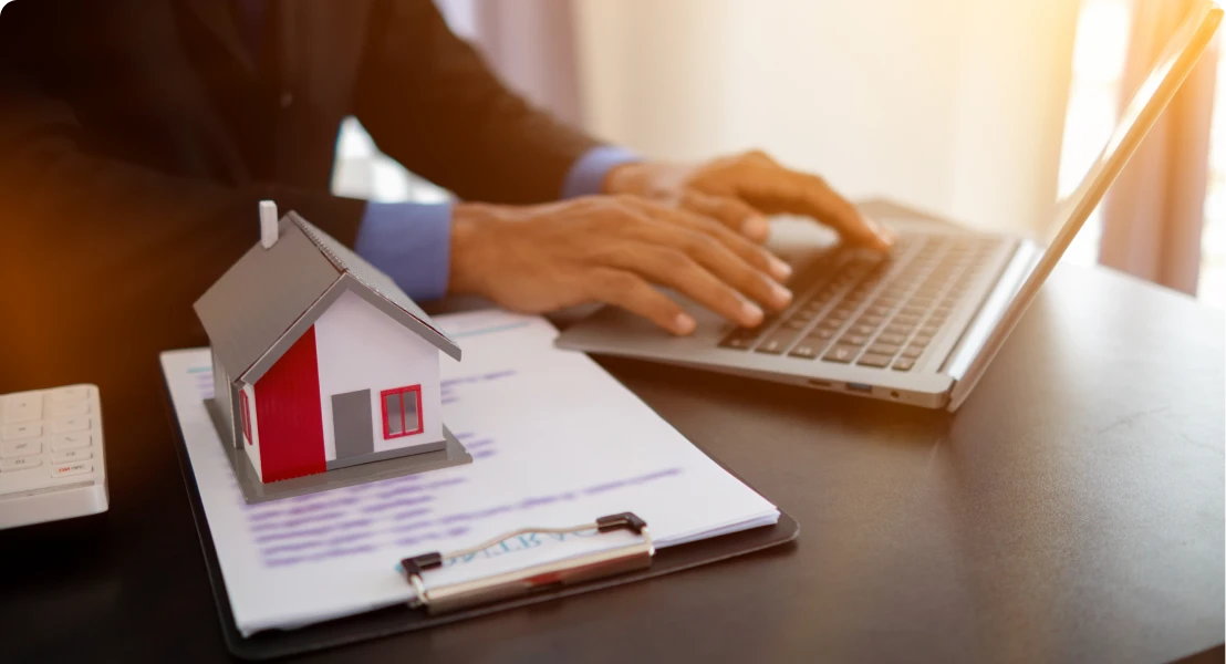Person typing on laptop near house model.