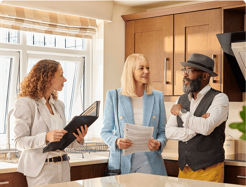 Three people discussing in a kitchen.